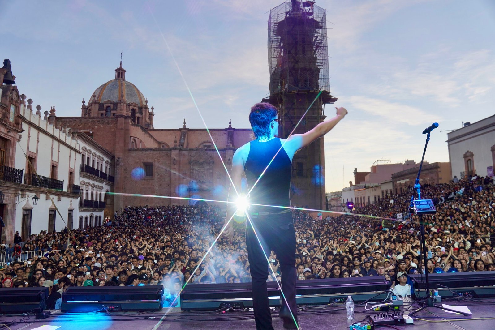 artista en escenario saludando a una multitud con una luz brillante detrás